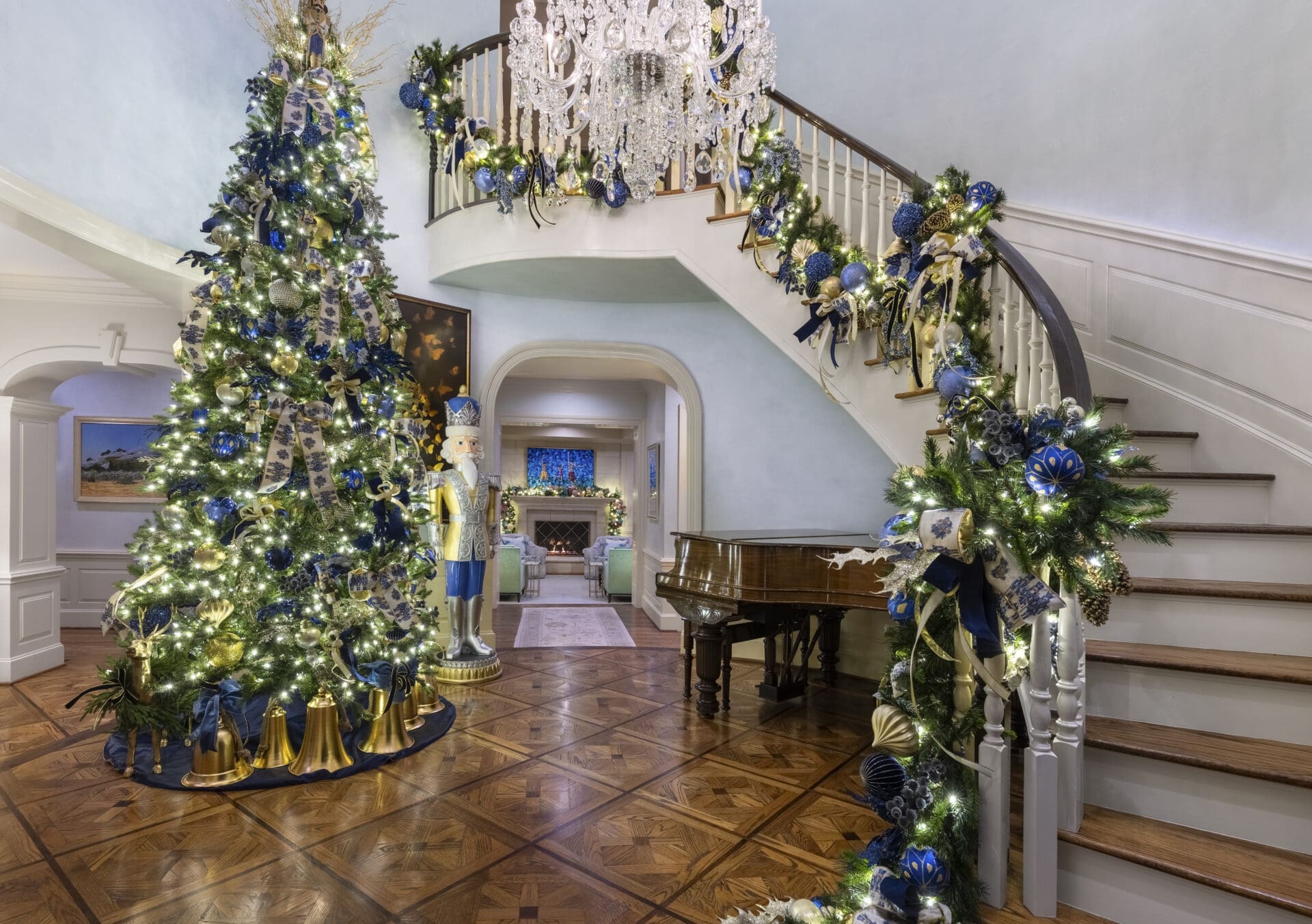 Grand holiday staircase decorated by Baker Design Group, featuring a lush lit garland alongside large-scale statement elements like oversized Christmas bells and classic nutcrackers.